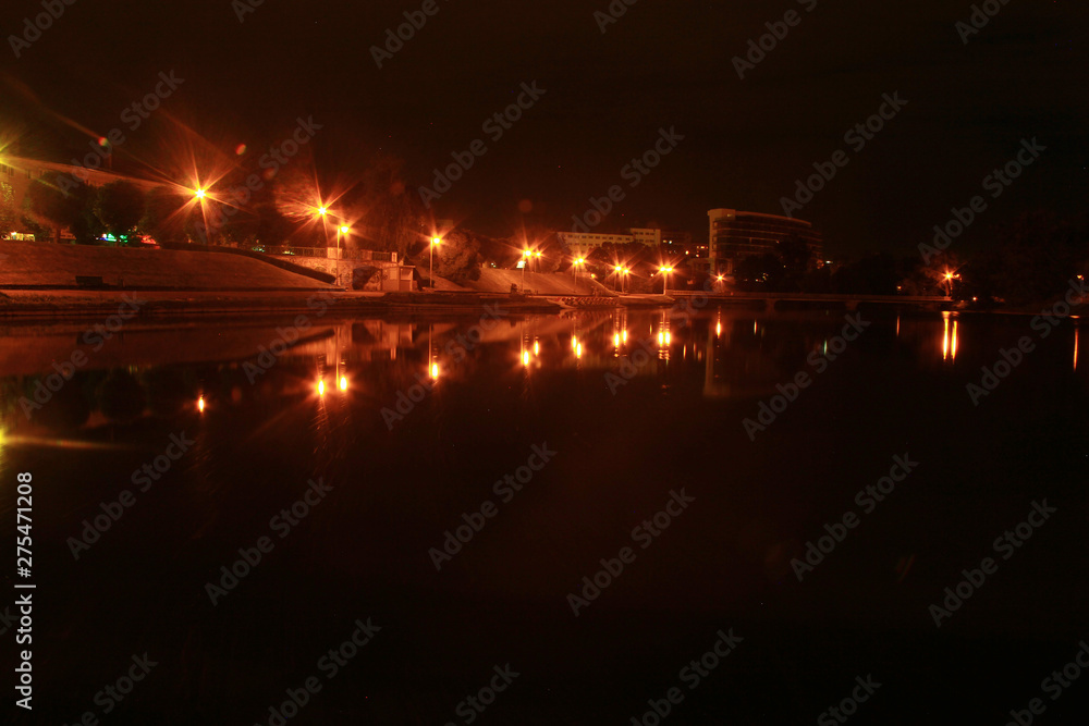 The dark water of the city lake at night reflects the lanterns of orange