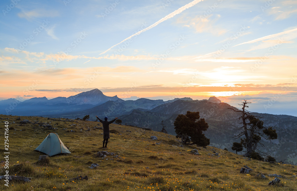 Hiker enjoying the summer sunrise while camping in the mountains.