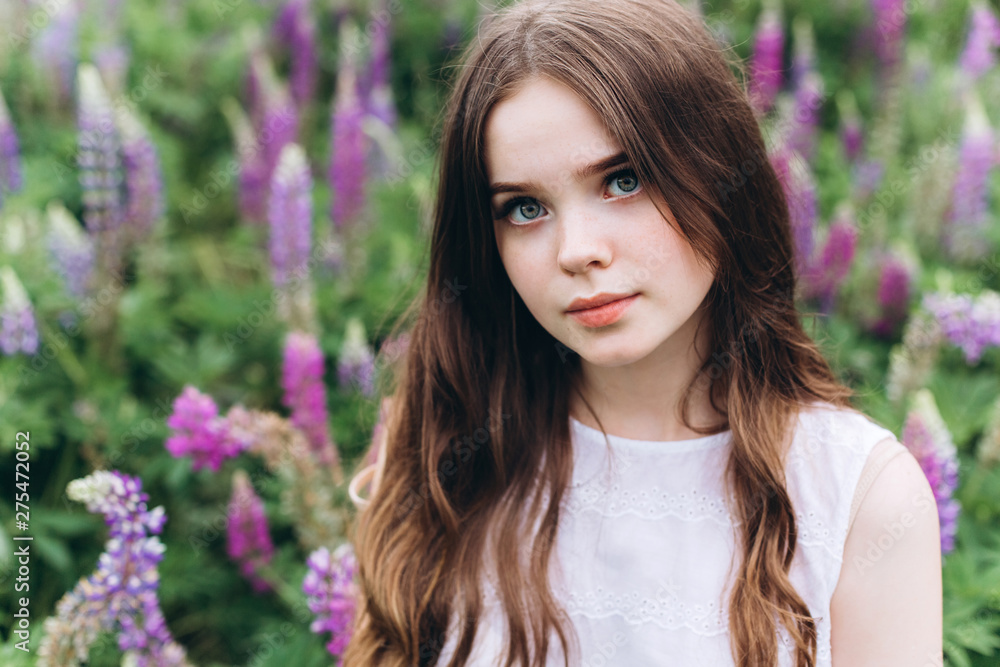 Portrait of young cute brunette girl in lupine violet field in blossom in summer sunset. Greenhouse, nature, natural beauty, freedom, youth concept Portrait of young cute brunette girl in lupine violet field in blossom in summer sunset. Greenhouse, nature, natural beauty, freedom, youth concept