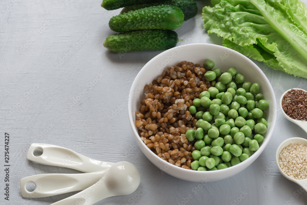 The concept of healthy food. Vegetarian breakfast. Bowl with spelled wheat and green peas, cucumbers, lettuce leaves, seasonings on gray background. The concept of healthy food. Vegetarian breakfast. Bowl with spelled wheat and green peas, cucumbers, lettuce leaves, seasonings on gray background.