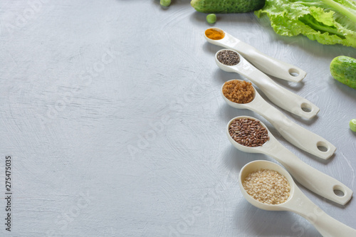 Natural food additives, spices in spoons: sesame, flax seed, chia, turmeric on gray background. The concept of healthy food.