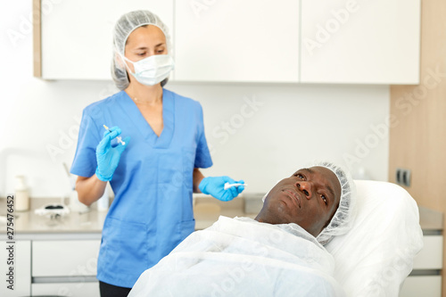 Cosmetician female preparing to aesthetic facial injection with man
