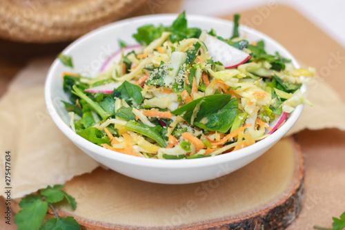 Fresh vegetable salad with greens and radishes, carrots and spinach leaves. Beautiful salad serving on the table, on a wooden stand in rustic style. Сoncept of healthy food, organic food, vegetarian