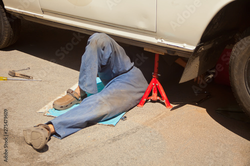 Photos Mechanic in blue dirty uniform lying down and working under car at auto service
