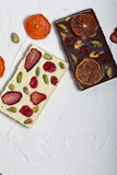 Homemade white and black chocolate. Decorated with slices of dried orange, strawberries, cherries and pistachios. On the surface covered with decorative plaster white.
