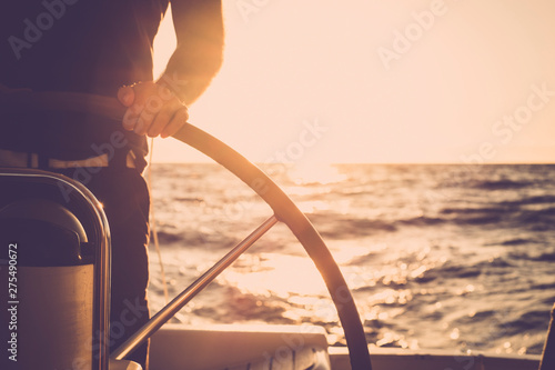 Close up of man's hand on sail boat helm - marine ship lifestyle concept of travel for beautiful holiday destination - alternative people life - sunset and sunlight in background on the ocean