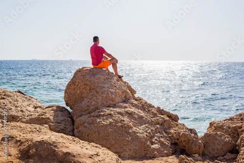 a man sits on a stone and looks into the distance on the blue sea