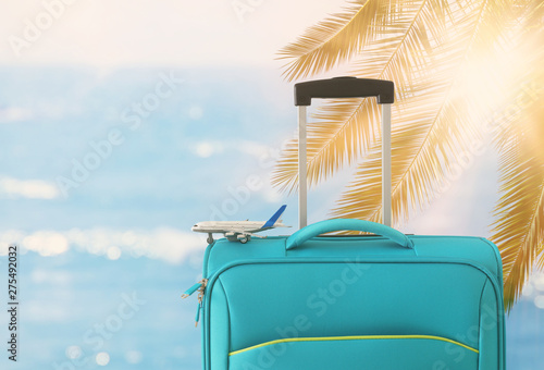 holidays. travel concept. blue suitcase and airplane toy infront of tropical background © tomertu