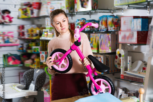 Young woman holding balance bicycle in the shop of goods for children