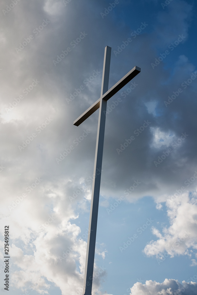 Large metal cross with blue sky and white clouds in the background Large metal cross with blue sky and white clouds in the background