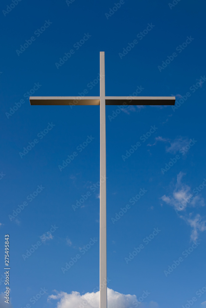 Large metal cross against blue sky background with parts of white clouds