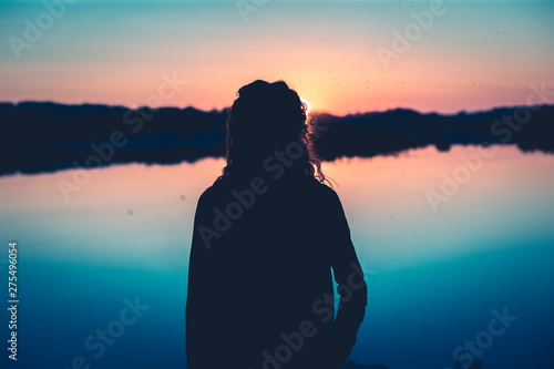 the warm summer sun gently illuminates the figure of a girl by the lake