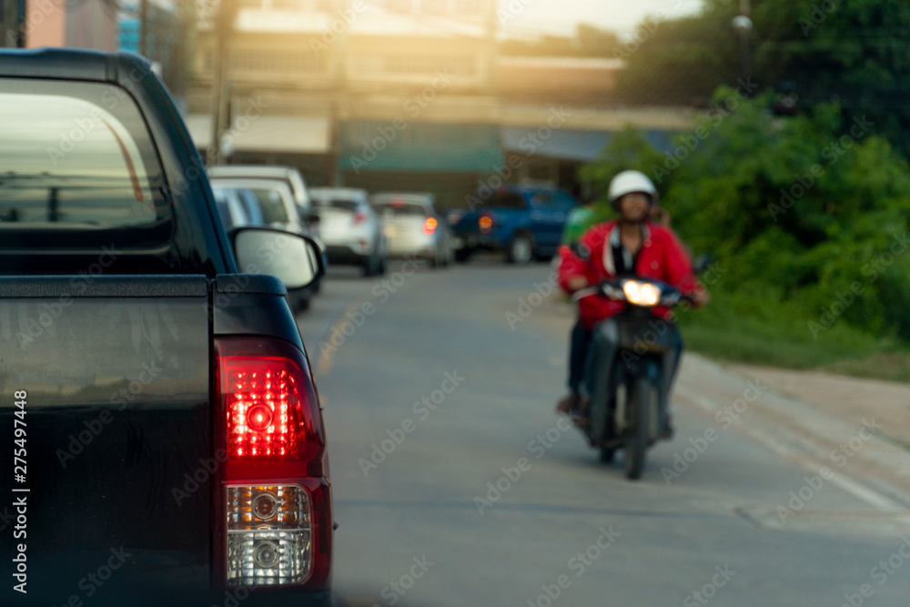 The black pickup truck parked on the traffic signal on the asphalt road and opened the brake light on the long queue.Blurred images of motorbikes, opposite lenses.