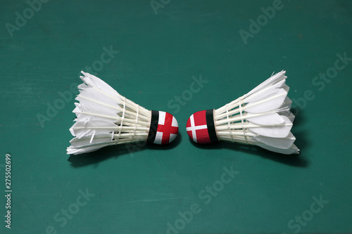 Two used shuttlecocks on green floor of Badminton court with both head each other. One head painted with England flag and one head painted with the Denmark flag.