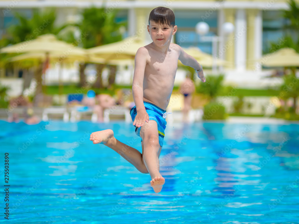 Boy spending time in pool at resort. He is jumping eagerly in to the swimming pool and enjoying his summer holidays.