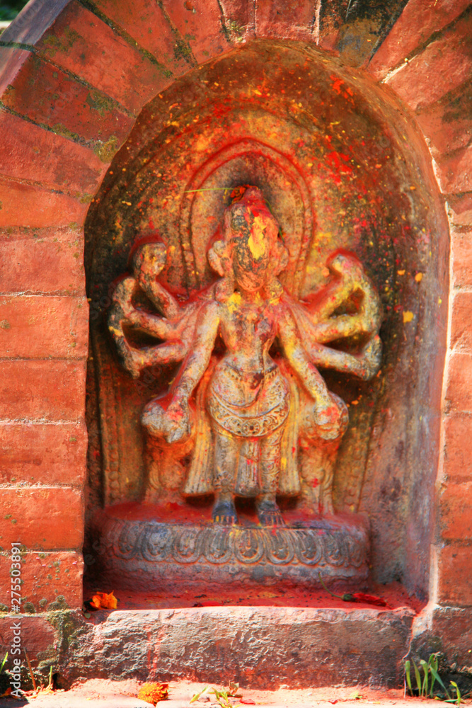 Shiva-Figur in einem kleinen Altar aus Stein in einem Hinterhof in Kathmandu, Nepal, Himalaya, Asien. Mit Farbpigmenten und Blumen geschmückt leuchtend orange und rot. Shiva-Figur in einem kleinen Altar aus Stein in einem Hinterhof in Kathmandu, Nepal, Himalaya, Asien. Mit Farbpigmenten und Blumen geschmückt leuchtend orange und rot.