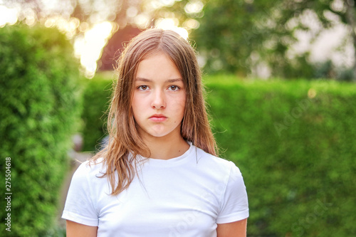 Bilde på lerret Close-up portrait of serious angry teenager girl outdoors in park with green hedge background