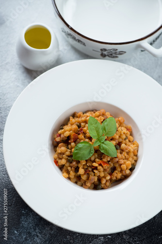 White plate with italian fregola pasta, high angle view over grey stone surface, vertical shot