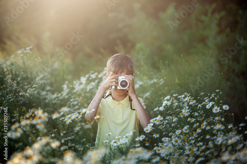Cute boy photographer shoots on camera in nature. Kid takes a photo in the camomile flowers field.