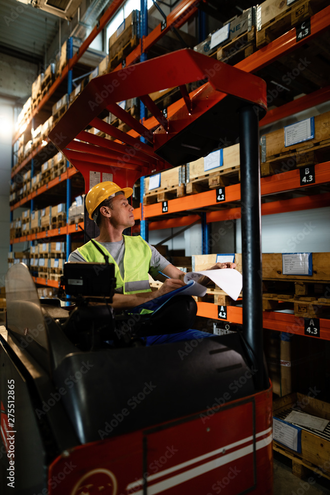 Forklift operator taking notes while working in a warehouse.