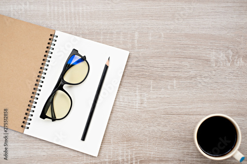 top view glasses and pencil place on open blank book,and coffee cup on wooden table.