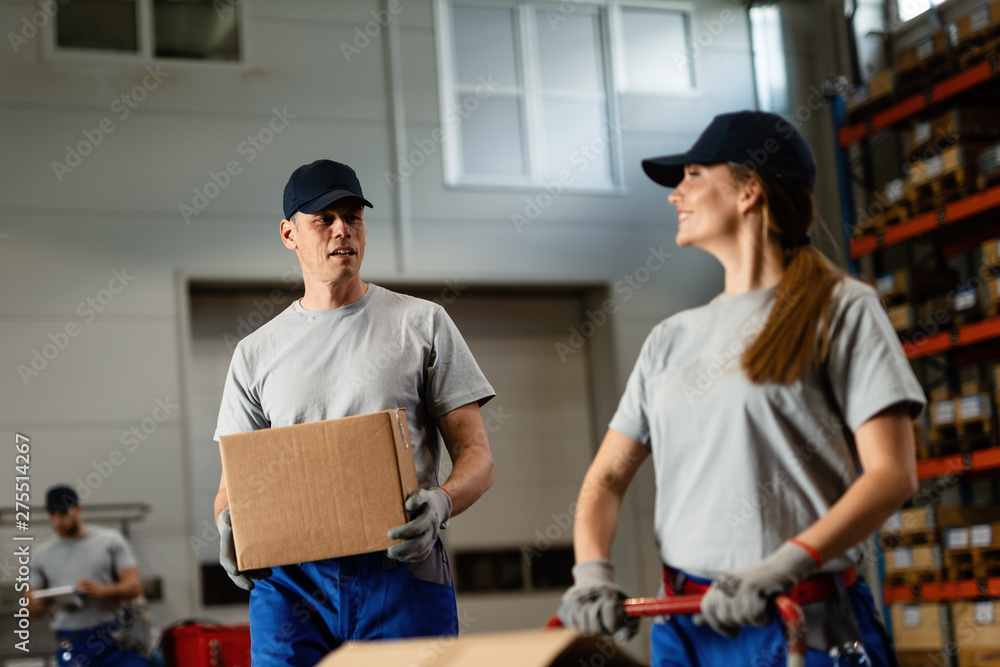 Two workers communicating while carrying packages in a warehouse. Two workers communicating while carrying packages in a warehouse.