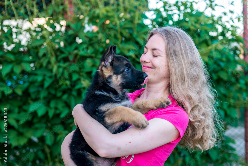 Portrait. Happy girl holding a small puppy German shepherd and smiles. Purchase and purchase of a dog, the joy of the first meeting with the animal. On a green blurred background with copy space Portrait. Happy girl holding a small puppy German shepherd and smiles. Purchase and purchase of a dog, the joy of the first meeting with the animal. On a green blurred background with copy space