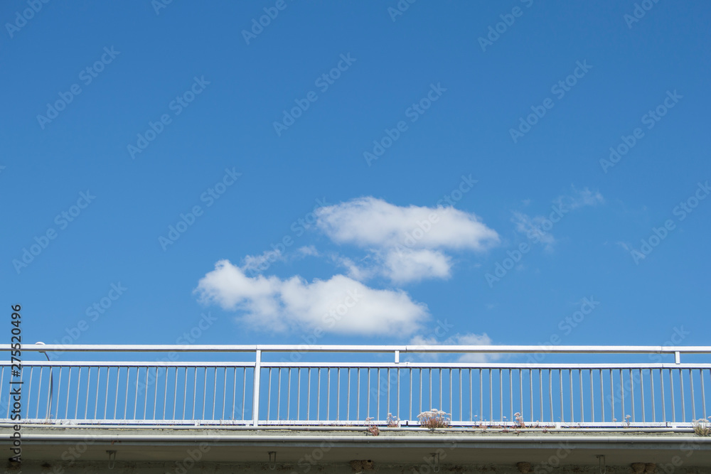 a handrail of a cut out bridge over a blue sky with clouds