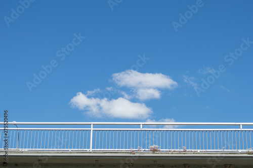 a handrail of a cut out bridge over a blue sky with clouds