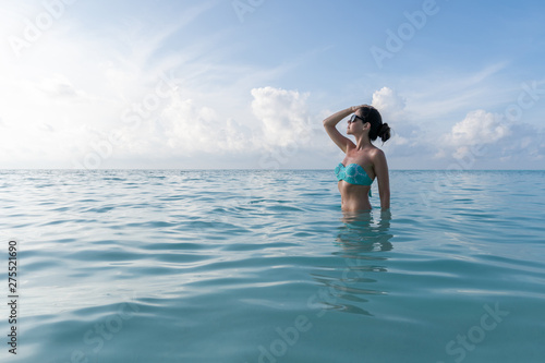 A young girl is standing to the waist in the turquoise water and looking toward the sun. © Raman