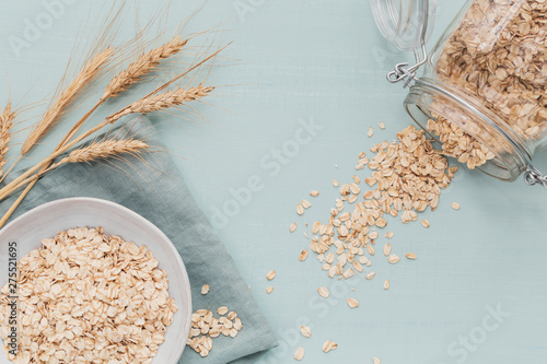 bowl of dry oat flakes with ears of wheat on light background. Cooking oats porridge concept