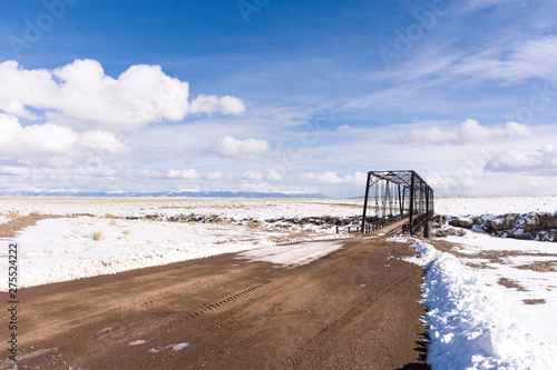 Costilla County  Colorado - February 21  2019  An 1892 wrought iron bridge spanning the Rio Grande in winter with snow  ice  blue sky  clouds. Built by the Wrought Iron Bridge Co. of Canton  Ohio.