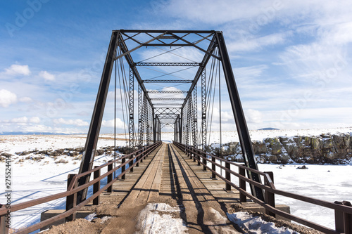 Costilla County, Colorado - February 21, 2019: An 1892 wrought iron bridge spanning the Rio Grande in winter with snow, ice, blue sky, clouds. Built by the Wrought Iron Bridge Co. of Canton, Ohio.