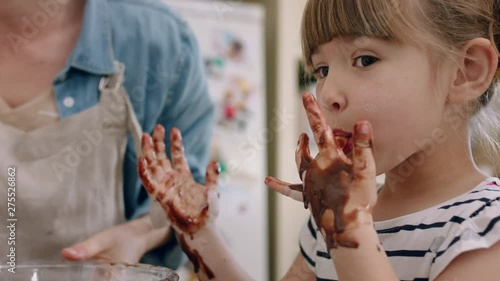 happy little girl with hands covered in chocolate licking fingers having fun baking in kitchen naughty child playing enjoying childhood photo