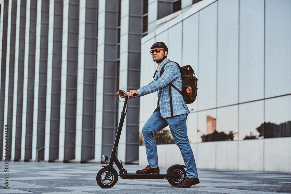 Cheerful modern man is driving his electro scooter near his office after long hard day. Cheerful modern man is driving his electro scooter near his office after long hard day.