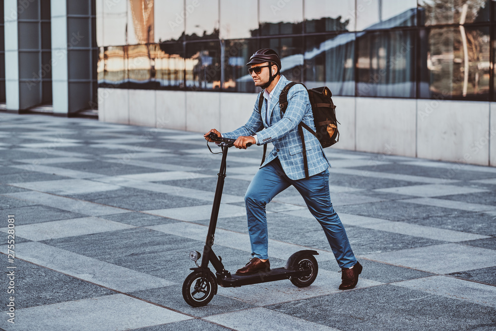 Cheerful modern man is driving his electro scooter near his office after long hard day. Cheerful modern man is driving his electro scooter near his office after long hard day.