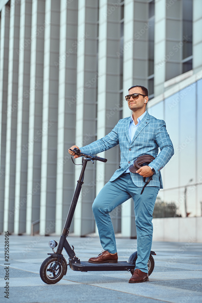 Cheerful modern man is driving his electro scooter near his office after long hard day. Cheerful modern man is driving his electro scooter near his office after long hard day.