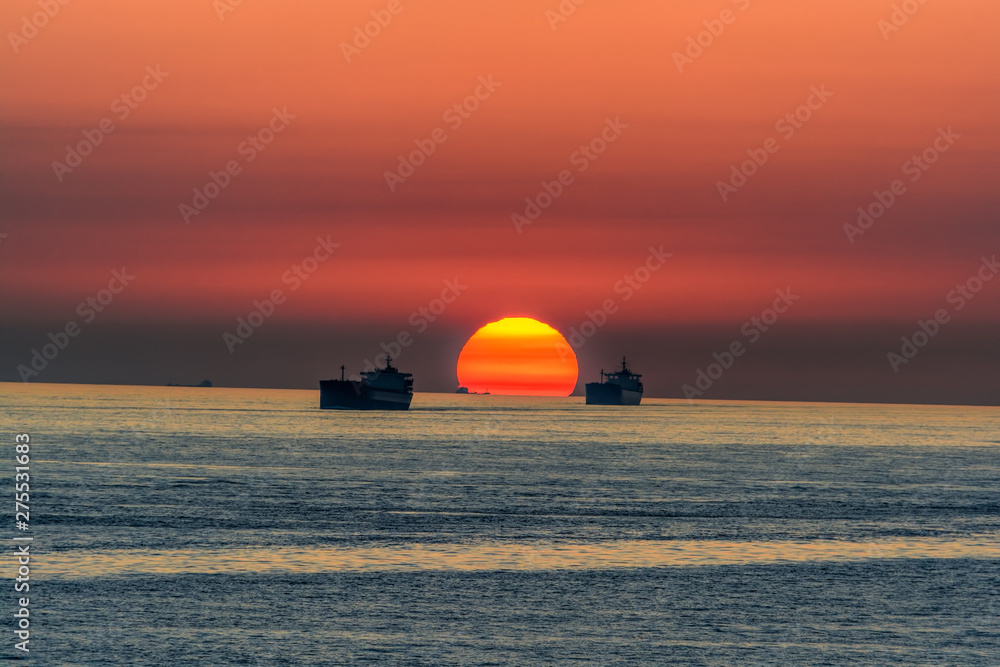 Incredible sunset over sea with a silhouettes of a cargo vessels.