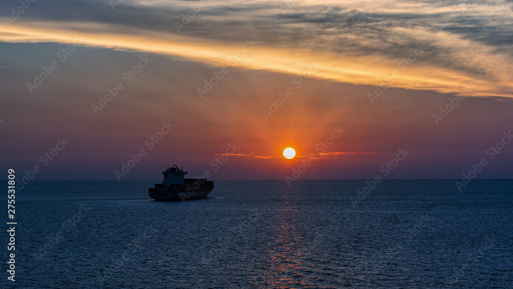 Incredible sunset over sea with a silhouette of a cargo vessel.