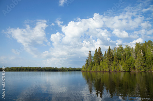 Northern Minnesota lake with trees along the shore and bright clouds on a calm morning