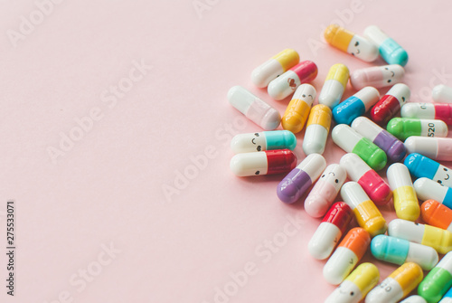 Pile of colored capsule and tablets on a pastel pink background