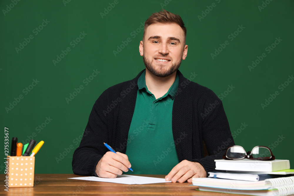 Portrait of young teacher at table against green background Portrait of young teacher at table against green background