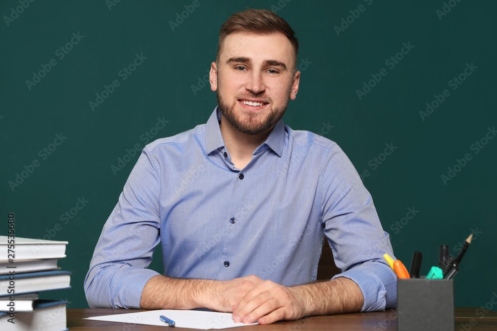 Portrait of young teacher at table against green background