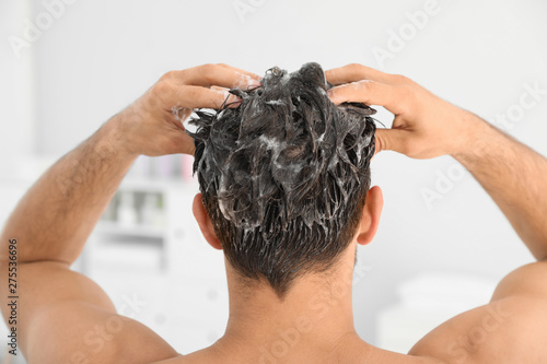 Man applying shampoo onto his hair against light background