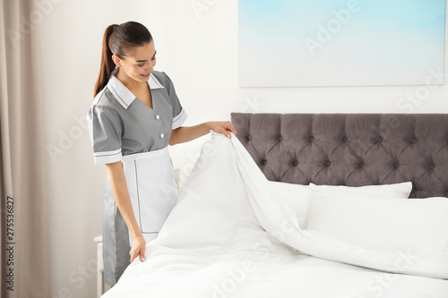 Young chambermaid making bed in hotel room. Space for text photo