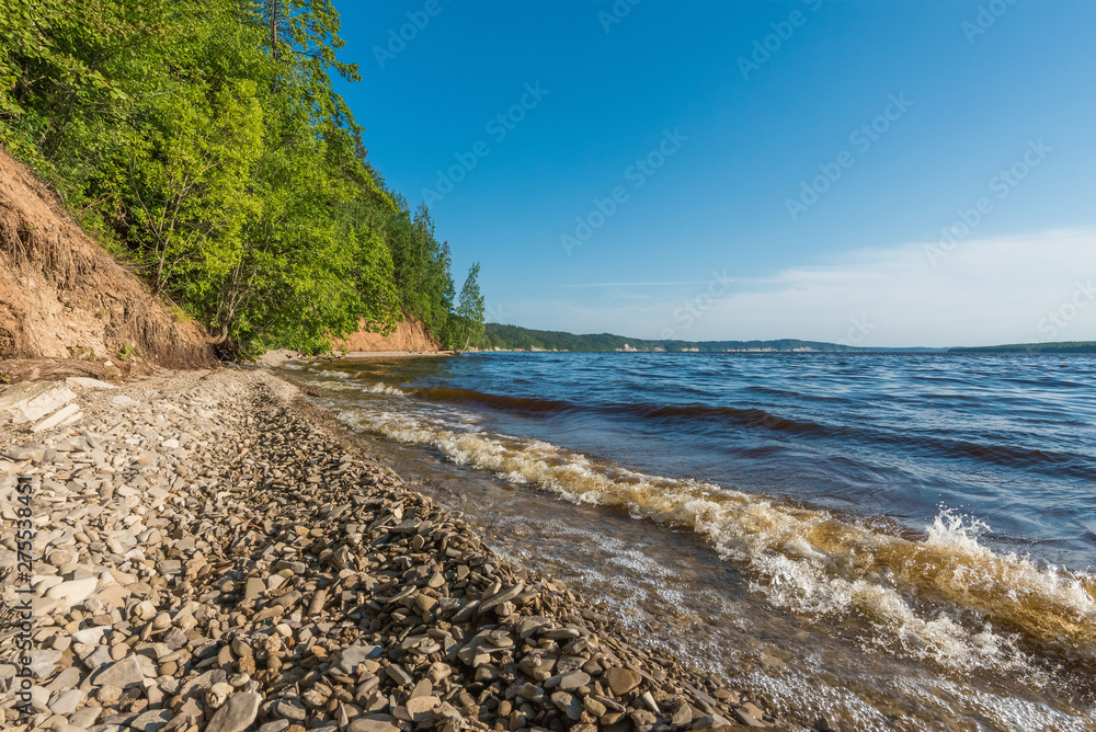 Kama river Bank in the summer afternoon with pebbles in the foreground and wave. Kama river Bank in the summer afternoon with pebbles in the foreground and wave.