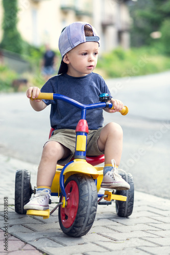 Boy on a three-wheeled bicycle in a cap with a visor. Shallow depth of field.