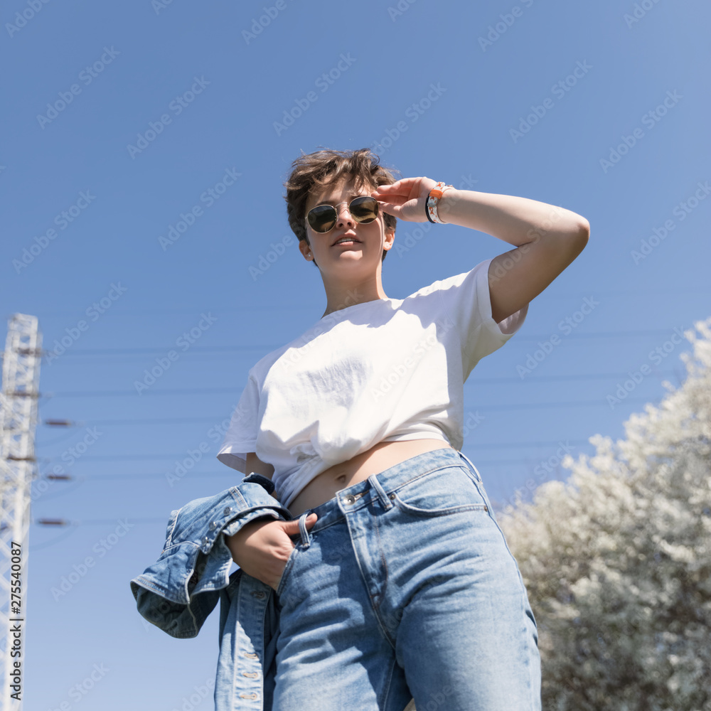 Young girl with a stylish short hair against the blue sky and a telecommunication iron tower. Conceptual photo about modern urbanization.