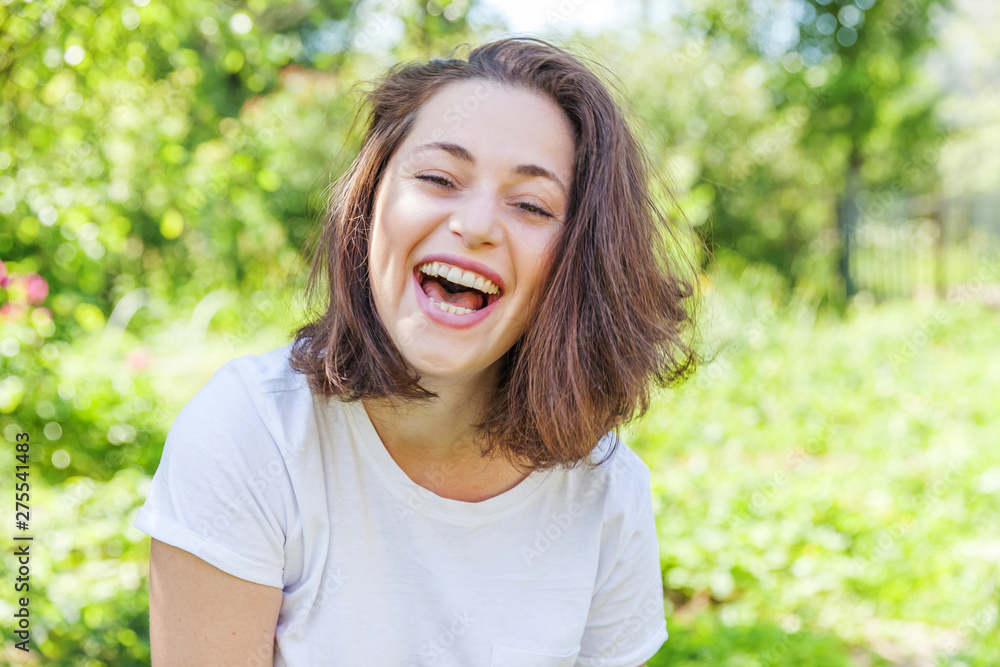 Happy girl smiling outdoor. Beautiful young brunete woman with brown hair resting on park or garden green background. European woman. Positive human emotion facial expression body language