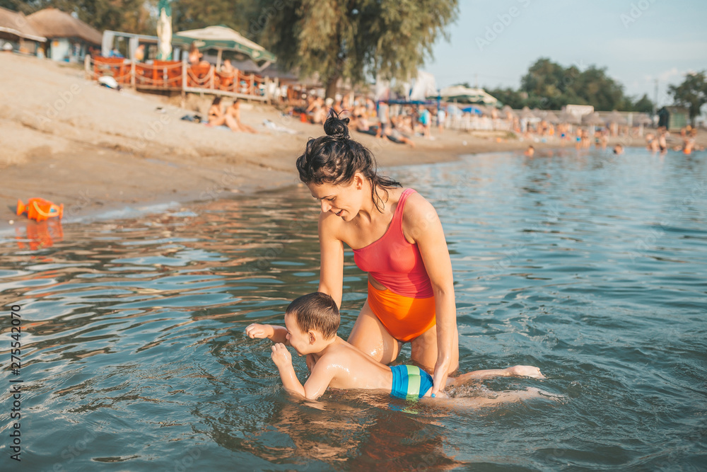Happy mother teaching her little son swimming in the water, on the beach